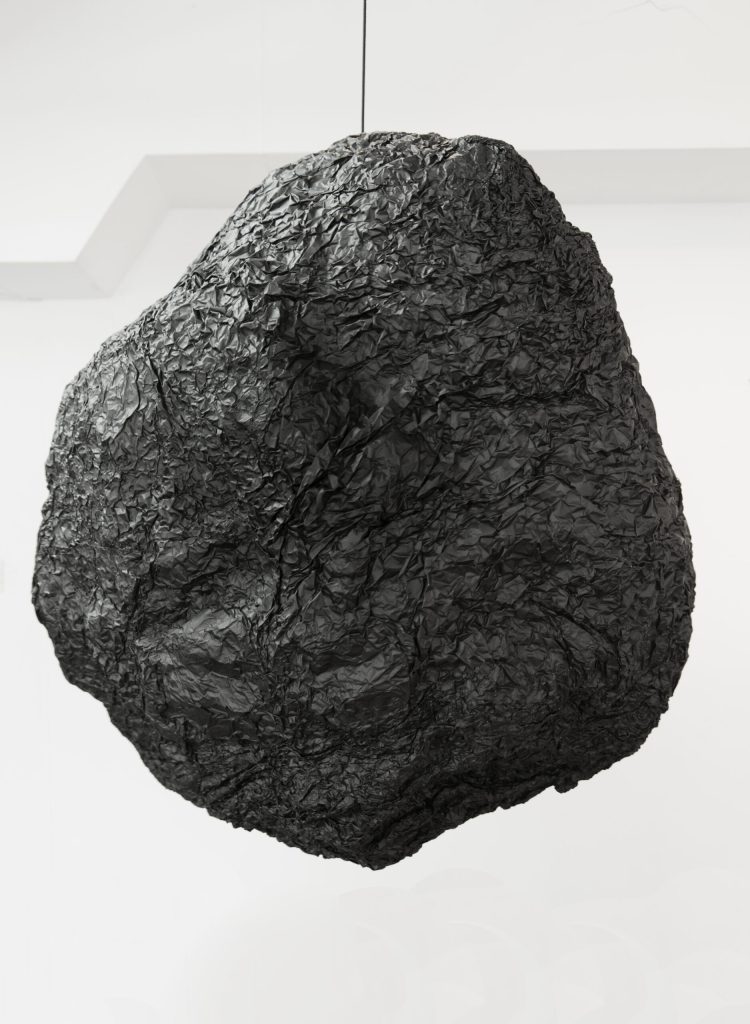 La producción de Basualdo despliega un imaginario que reflexiona acerca de la tensión entre el lenguaje y el cuerpo como constructores de realidad. El artista utiliza ficción para expandir cartografías, generar territorios donde parece que solo hay una línea. Su trabajo convoca a lx expectadxr a una experiencia en tiempo presente; sus obras dan idea de un inestable equilibrio a punto de quebrarse y, en ocasiones, convocan al riesgo como amplificador de los sentidos. Los principios que rigen el espacio, el cuerpo y la razón entran en diálogo para configurar una experiencia de libertad, en un sentido físico y filosófico. Las instalaciones de Basualdo se asemejan a paisajes de enorme tensión dramática que invitan al público a ser protagonista de una ficción palpable. El artista aborda la categoría de lo sublime en una clave oscura donde lx espectadxr es cautivx de una imagen imponente a la vez que se encuentra a la expectativa de un desenlace que nunca llega. El peligro y la curiosidad se debaten en contradicción. En sus piezas escultóricas, a veces incluidas en sus instalaciones, el artista trabaja con objetos cotidianos, como vasos, cuchillos y velas que, puestos en una relación inquietante entre sí y con el espacio, adoptan un carácter simbólico y siniestro. Estas piezas suelen incluir una dimensión del sonido, en general, emitido por los propios objetos en secuencias aleatorias. Entre los materiales más recurrentes en su producción, se encuentra el black foil, utilizado en el ámbito de la iluminación teatral, que le permite producir enormes volúmenes rugosos en sus piezas escultóricas y que, a la vez, aporta un elemento de contradicción entre su tamaño y su liviandad. Con él genera tanto piezas colgantes como formas gigantescas que llegan ocupar salas enteras. En sus dibujos, la línea, el doblez y el corte aparecen de manera recurrente poniendo en tensión la dimensión del soporte físico con la del pensamiento.