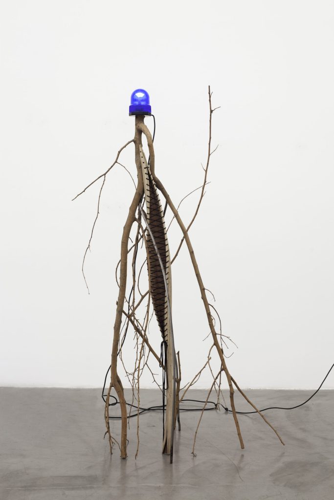 La producción de Telleria revela una considerable diversidad de recursos y operaciones artísticas que destilan y metabolizan reflexiones profusas, como la significación cultural de las cosas cotidianas, las posibilidades de uso que ofrecen las formas y el modo en que toda civilización se define por un abordaje particular de las relaciones entre naturaleza y construcción, capaces de manifestarse en terrenos tan disímiles como la metafísica, la cosmogonía y la moda. Es medular a su práctica la intención de subvertir aquello que existe, guiada siempre por la posibilidad de generar sincronías entre cosas, formas y sentidos lejanos. Las ideas están en todos lados y, como sucede en la construcción de un poema, del mundo o la realidad; los elementos que los conforman actúan como fuerzas que pueden confluir y reordenarse, contagiarse entre ellas, torcer lo derecho, juntarse con un objeto de otro orden material y explorar configuraciones insospechadas. Las intuitivas intervenciones y transformaciones que realiza sobre las cosas evidencian un archivo de sentidos desacralizados que conforman su patrón poético y conceptual, en el cual la iconografía religiosa comparte con la basura, la moda, el accidente, el espectáculo, la industria y la naturaleza una misma jerarquía horizontal. Oscilando entre la abstracción y la figuración, rebotando entre el surrealismo y el conceptualismo, la artista nos enfrenta a un colapso epistemológico. Telleria habita su práctica artística como una metafísica alternativa en la que pueden plantearse nuevas relaciones ambientales, antropológicas e interespecie. En este territorio de temperamento hereje que la artista construye, cualquier objeto, espacio o situación es propenso a ser explotado en su dimensión estética, una suerte de purga milagrosa de sentido que renueva todas las cosas: marcos, camas, imágenes religiosas y autos son cortados en cuatro para convertirse en cruces, las cruces son mástiles, las ramas bichos y las ruinas de una catástrofe devienen monumento. La idea del color negro, la insistente aplicación material del negro ya es parte del patrimonio de la artista, tanto como intervenir en la aparente permanencia de las cosas. Así sus instalaciones e intervenciones en el espacio público irrumpen en el paisaje de lxs transeuntxs, forzandolxs a preguntarse por aquello que desestabiliza su mirada habitual. Le interesa ese interlocutor eventual, ajeno a cualquier entidad legitimadora, abandonadx a su propia reflexión estética y ontológica en un entorno proclive a la ambigüedad, donde se sacrifica el yo de la artista. En esa voluntad que se vuelve anónima Telleria reconoce el estímulo radical de la relación entre lo público y lo privado, el adentro y el afuera.